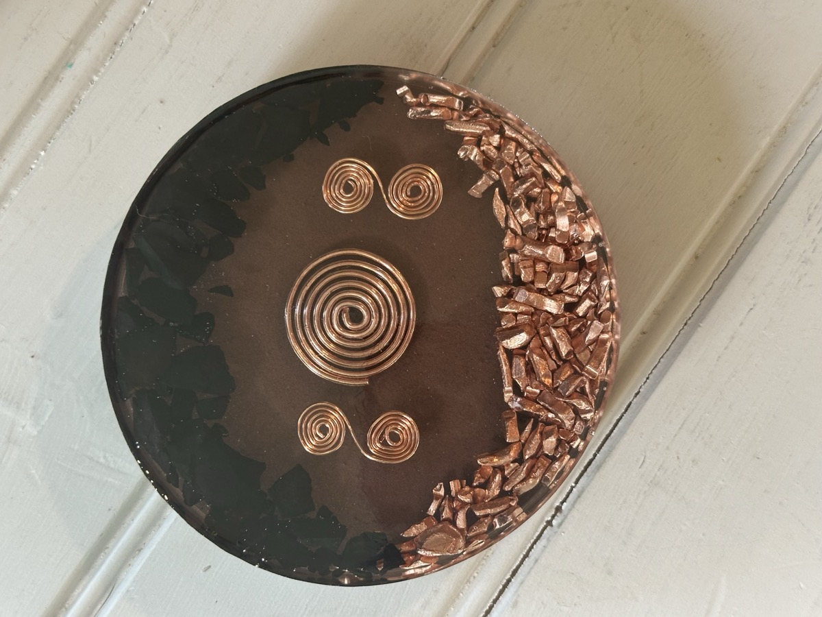 Handmade orgone coaster with center copper coil and two flanking spirals in dark resin with shungite