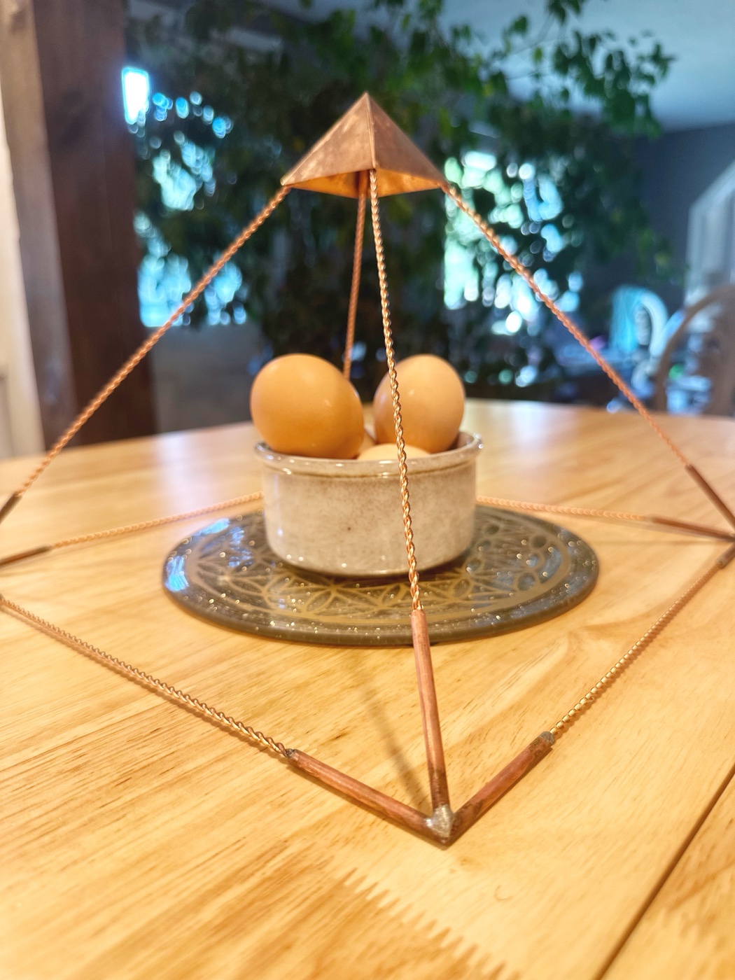 Handmade copper wire pyramid frame with twisted edges and solid copper cap on a wooden table.