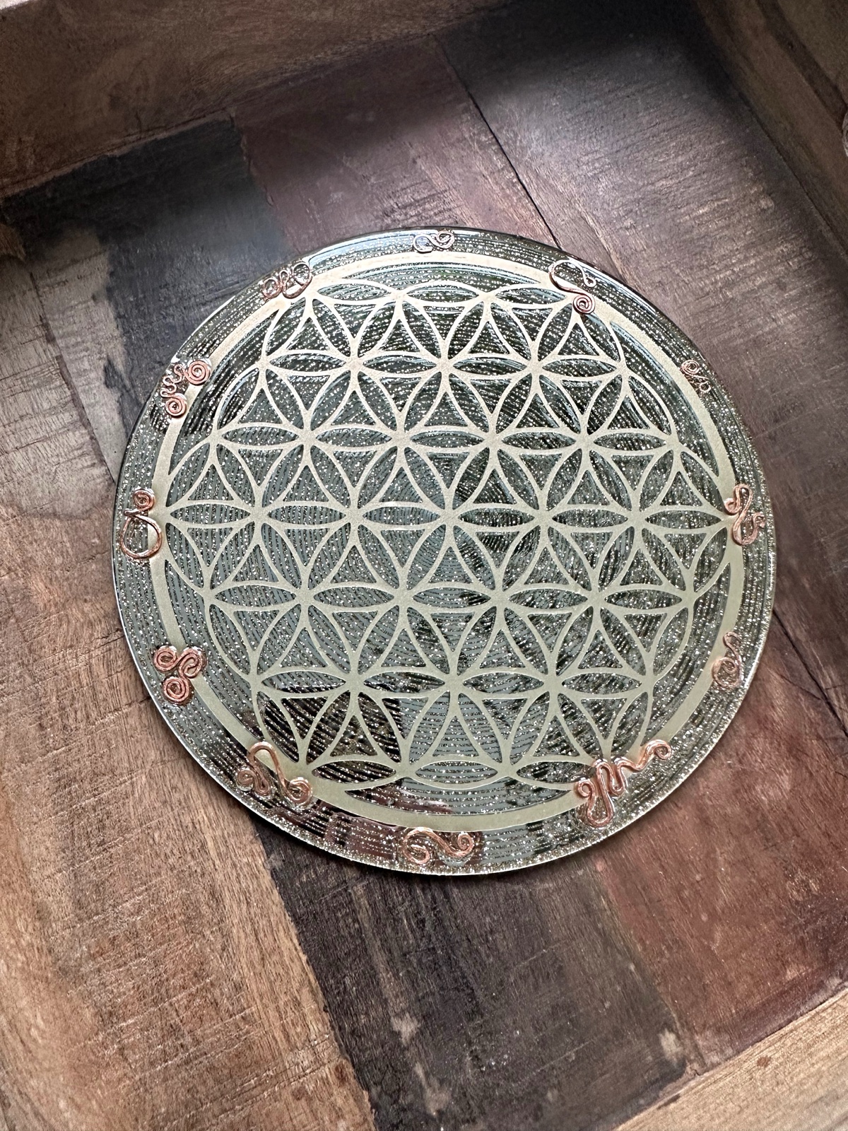 Handmade 8 inch mirror glass charging plate with Flower of Life sacred geometry and copper triskelion edge on dark wood
