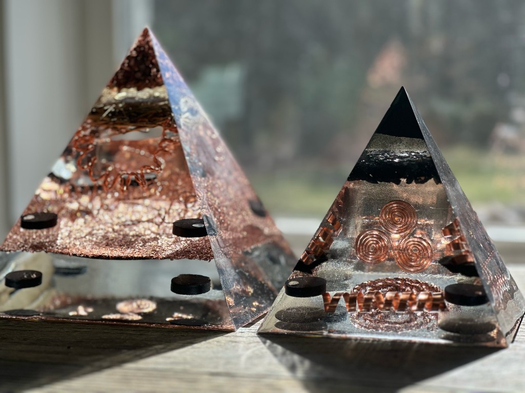 Two handmade orgonite pyramids with copper spirals backlit by a window