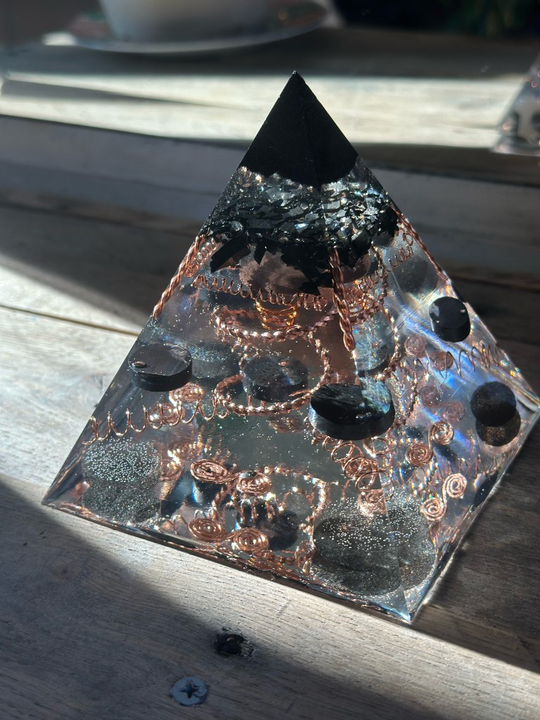 Handmade small orgonite pyramid with shungite cap, copper coils, and shungite discs in sunlight
