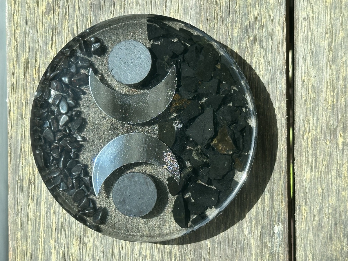 Double crescent moon design in copper on dark resin with shungite, hematite, and iron filings.