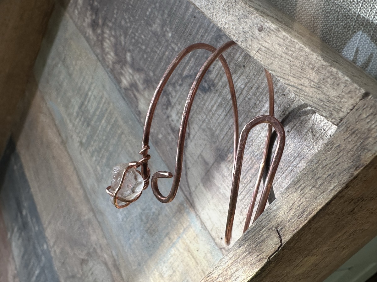 Handmade copper bracelet with wire-wrapped sea glass, photographed on a natural wood surface