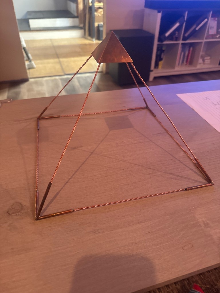 Handmade copper wire pyramid on a wood table, twisted copper edges with solid copper cap