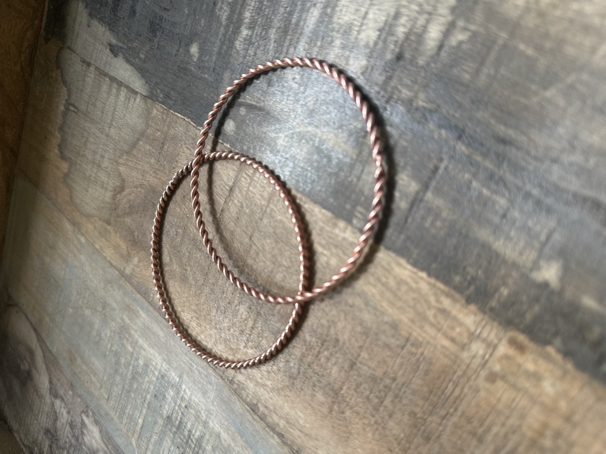 Handmade copper tensor rings twisted from cubit-length wire, viewed from above on dark wood