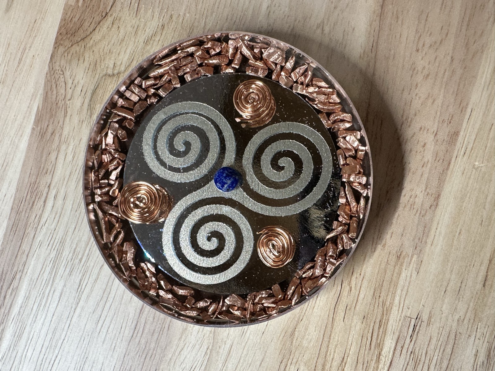 Silver triple spiral on mirrored black resin with copper chip border, compass spirals, and lapis center.