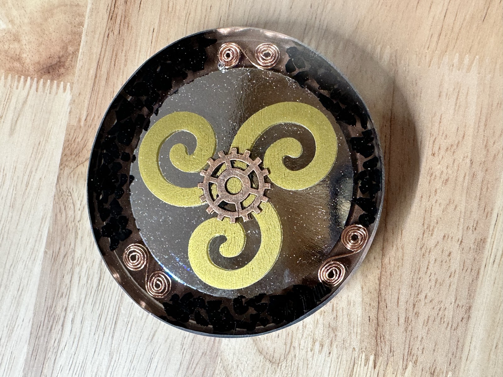 Gold two-armed spiral on mirrored black resin with shungite chip border and brass gear center.